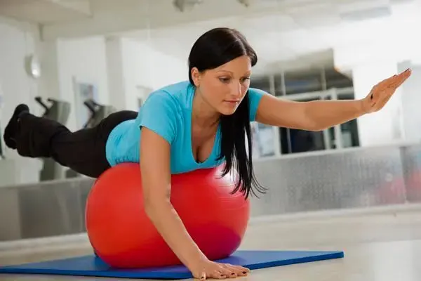 A patient performing a balance exercise over a therapy ball in a rehabilitation room